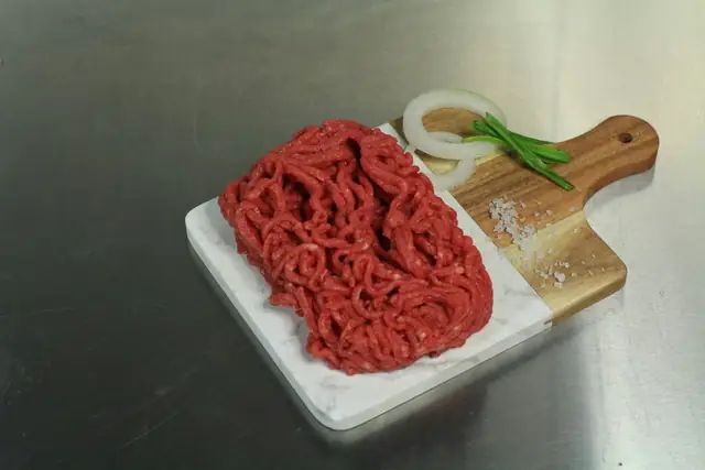 Carne molida cruda presentada sobre una tabla con cebolla y chile.